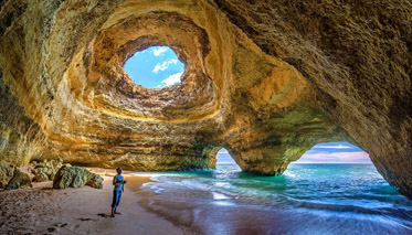Eine Person steht in einer felsigen Höhle am Meer an der Felsalgarve in Portugal