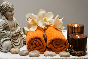Zusammengerollte Handtücher neben Kerzen und einer Buddhafigur
